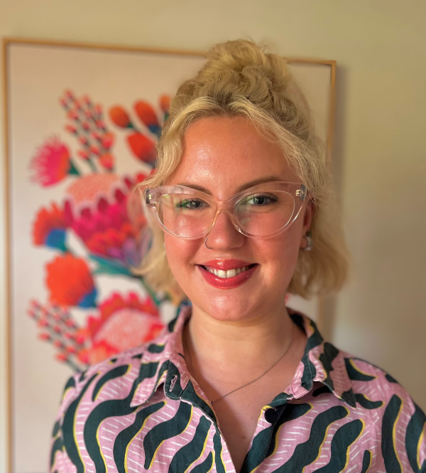 Photo of Alyce, who has short blonde hair and is wearing glasses and smiling at the camera.