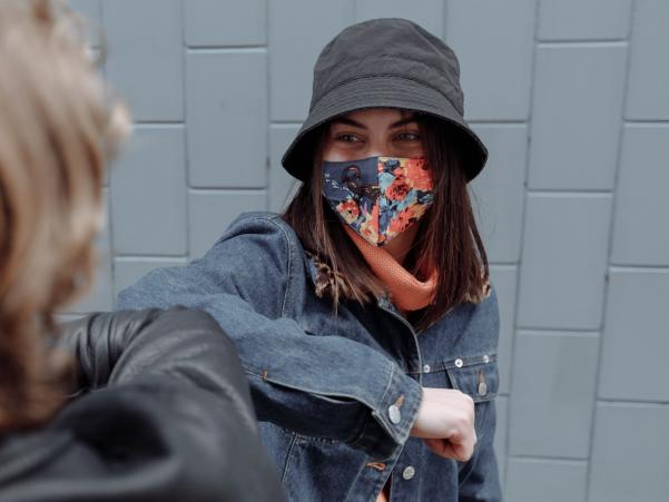 A person wearing a colourful face mask touching elbows with another person