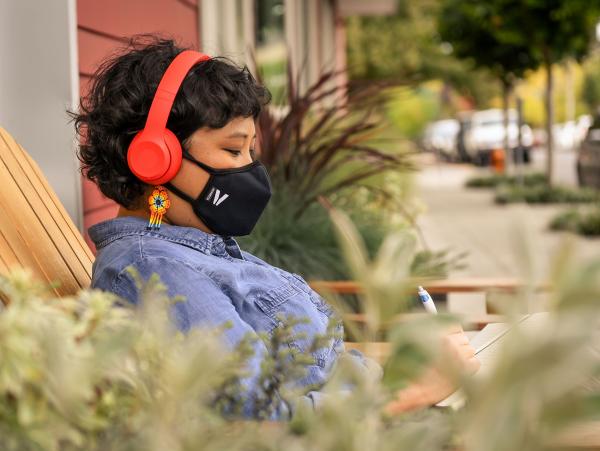 Close-up of a Filipinx woman wearing headphones and a filtering face mask