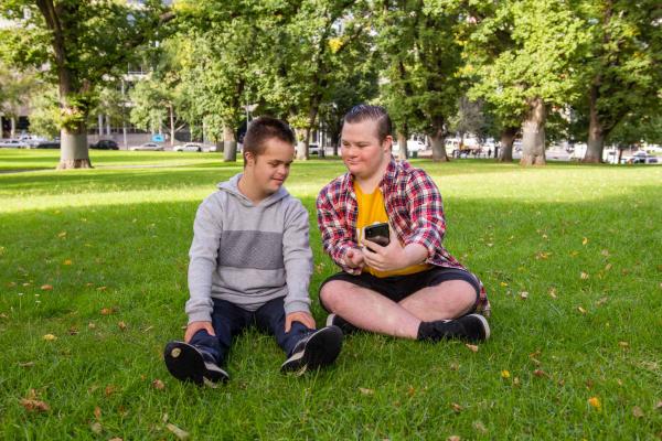 Two teenagers sitting on the grass at a local park. They are looking at a phone.