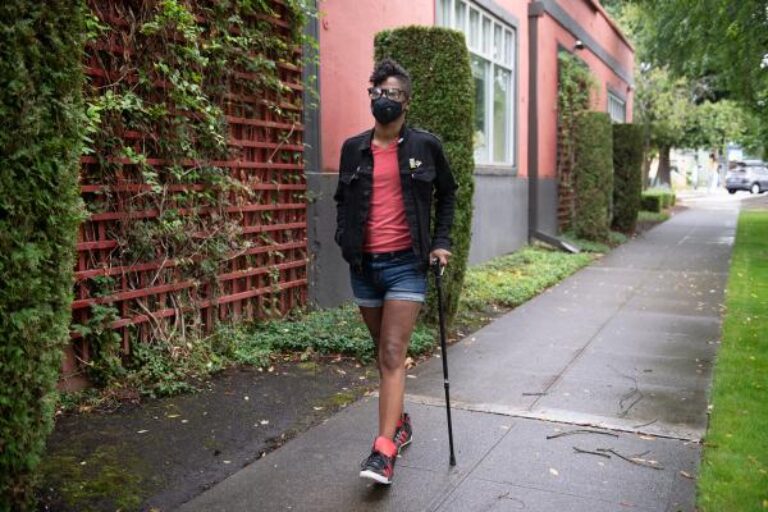Person walking outdoors with a walking stick. They are wearing a Vogmask.